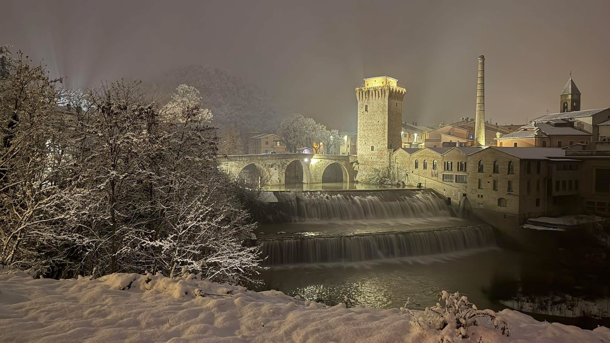 L'Ex Lanificio Carotti e la cascata del Metauro innevati di notte, con la torre illuminata: atmosfera invernale per la cena aziendale di dicembre