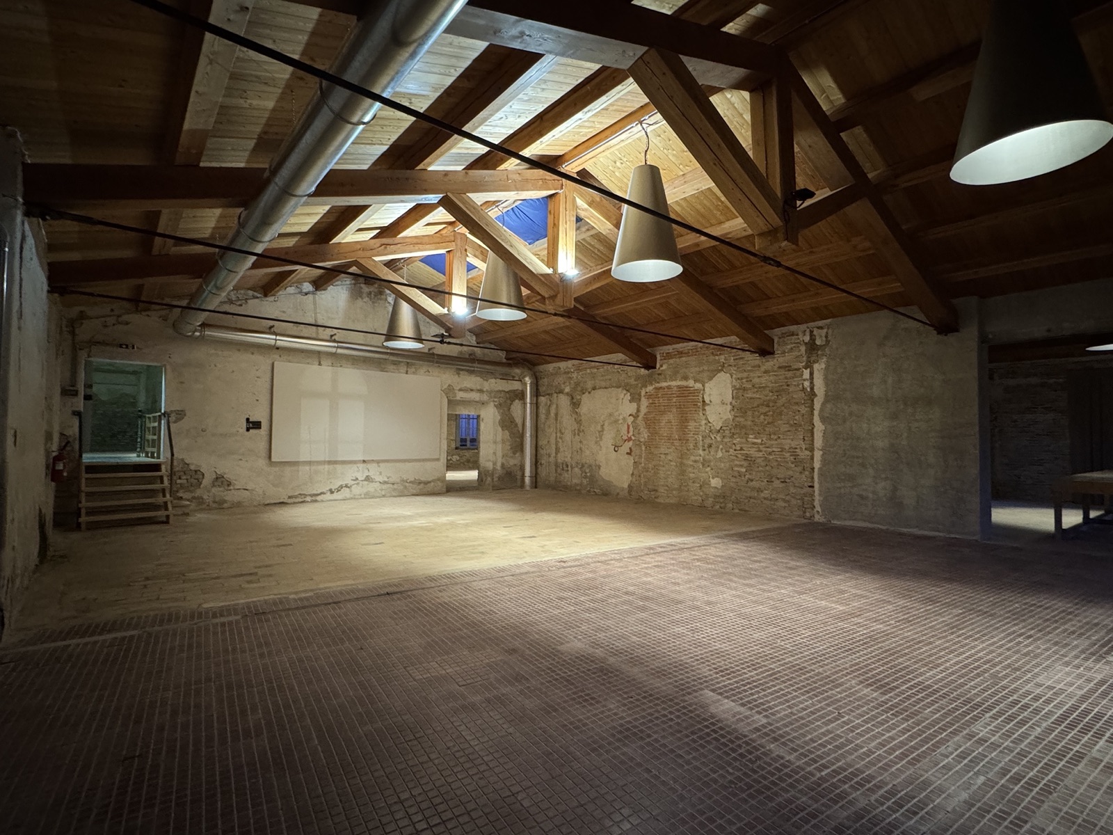 Sala della filatura all'Ex Lanificio Carotti, con capriate in legno, lucernario e lampade industriali sospese