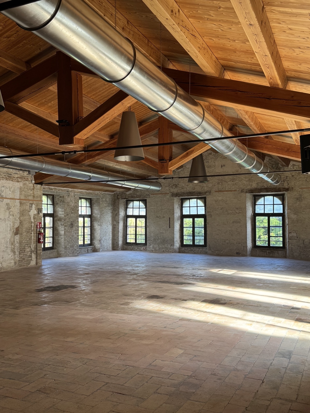 Sala della tessitura vuota nell'Ex Lanificio Carotti, con finestre ad arco affacciate sul Metauro e ampia luce naturale