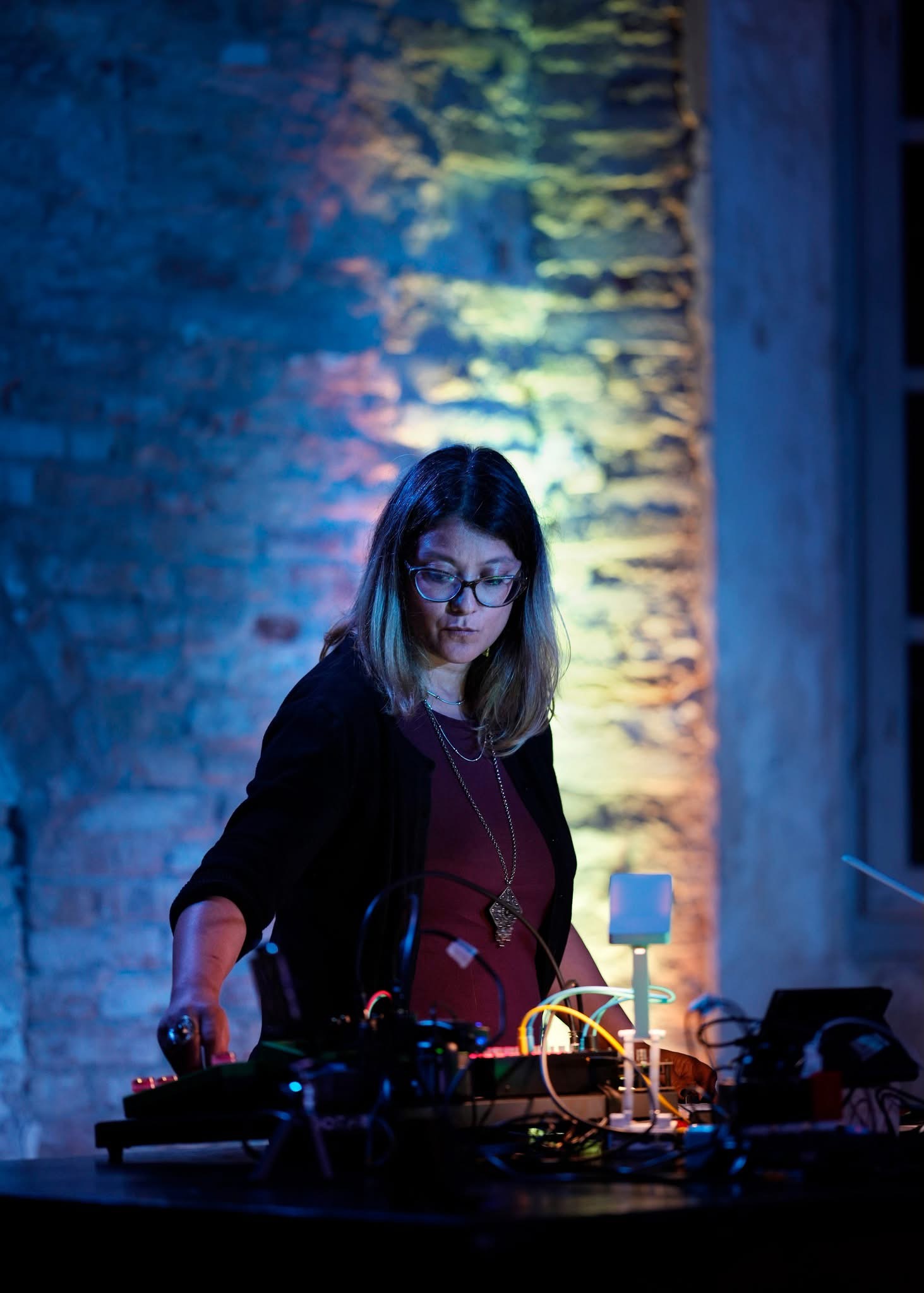 Una musicista al tavolo dell'elettronica dal vivo, tra le pareti in mattone a vista dell'ex lanificio