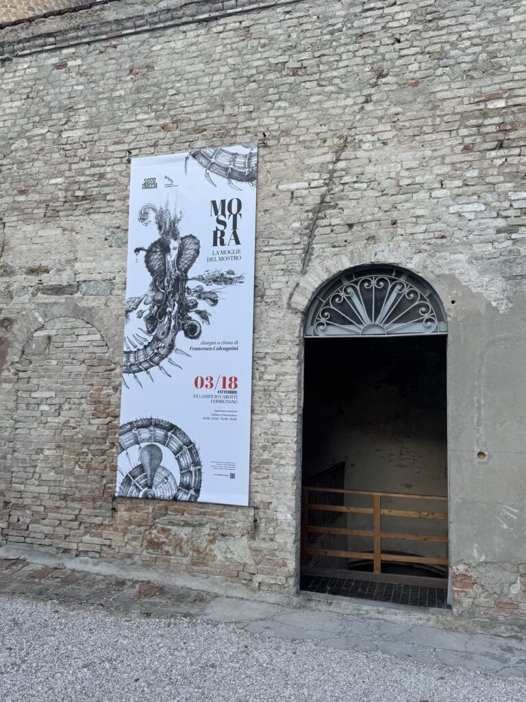 Il banner della mostra appeso al muro in pietra all'ingresso del lanificio.
